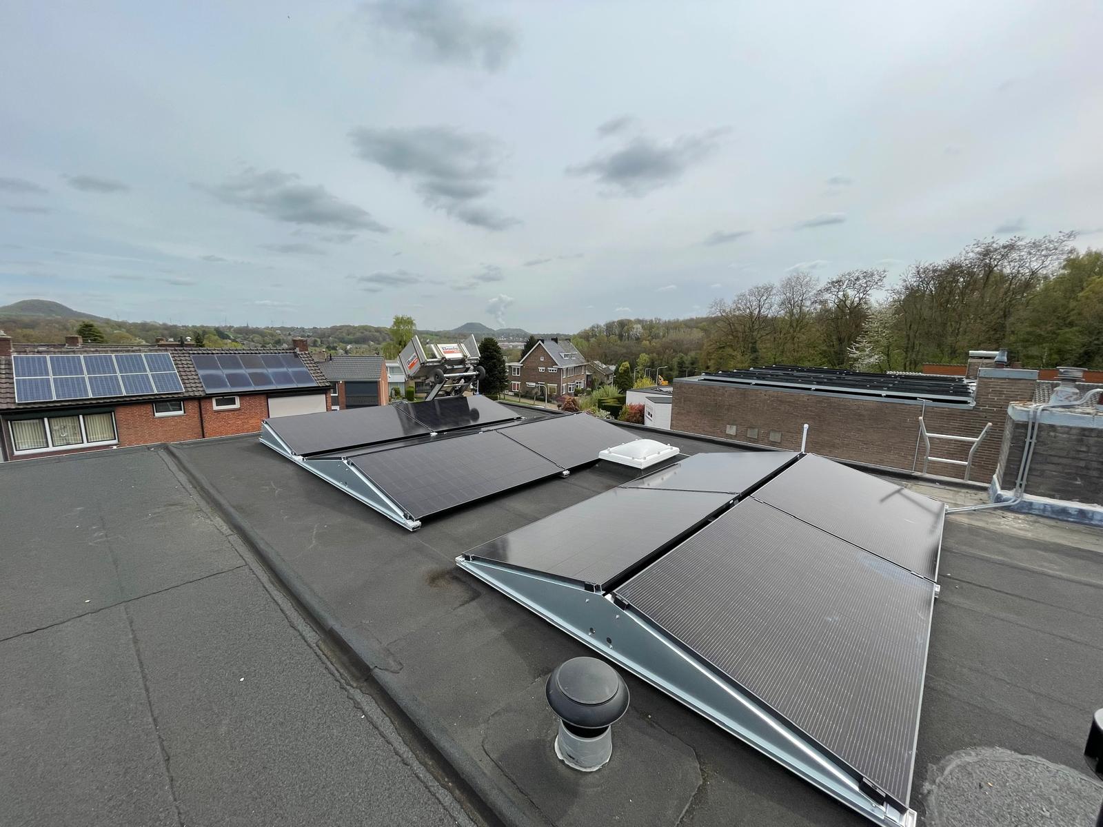 Zwarte zonnepanelen in schuine opstellingen op een hoger gelegen plat dak, met een ladderlift op de achtergrond.
